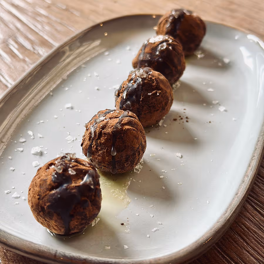 Cinc boletes de xocolata amb cacau i escates de sal sobre un plat blanc allargat.