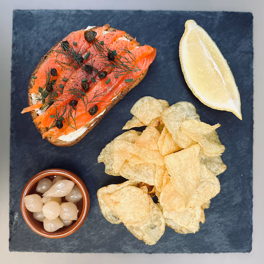 Llesca de pa amb salmó fumat, enciam i tàperes, patates fregides, ceba en vinagre i un tros de llimona.