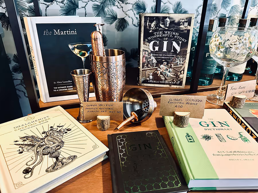 Taulell amb llibres de còctels i ginebra, coctelera i copa decorada amb flors.