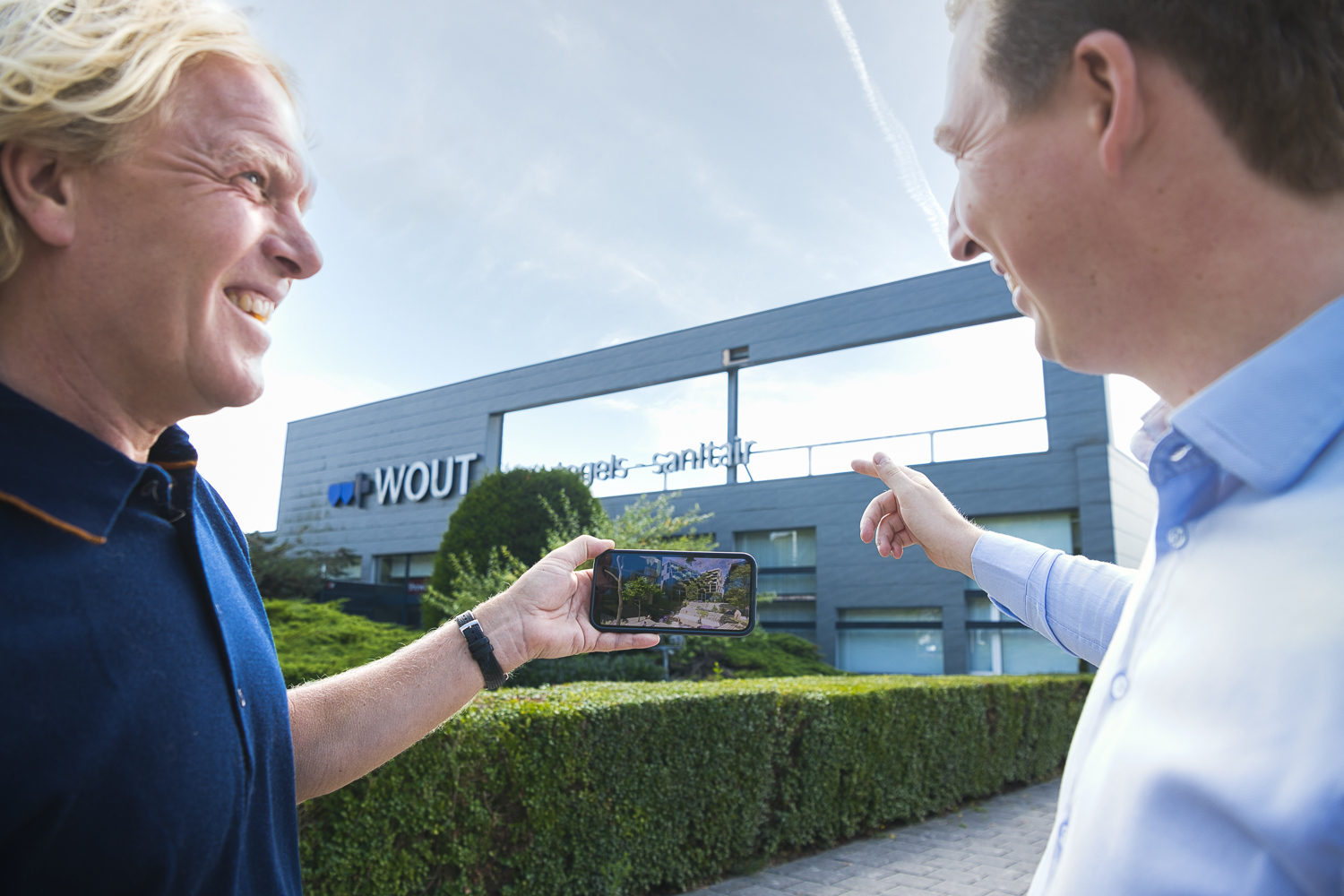 Twee ontwikkelaars met telefoon in handen voor het gebouw vanTransformatie Project Wout