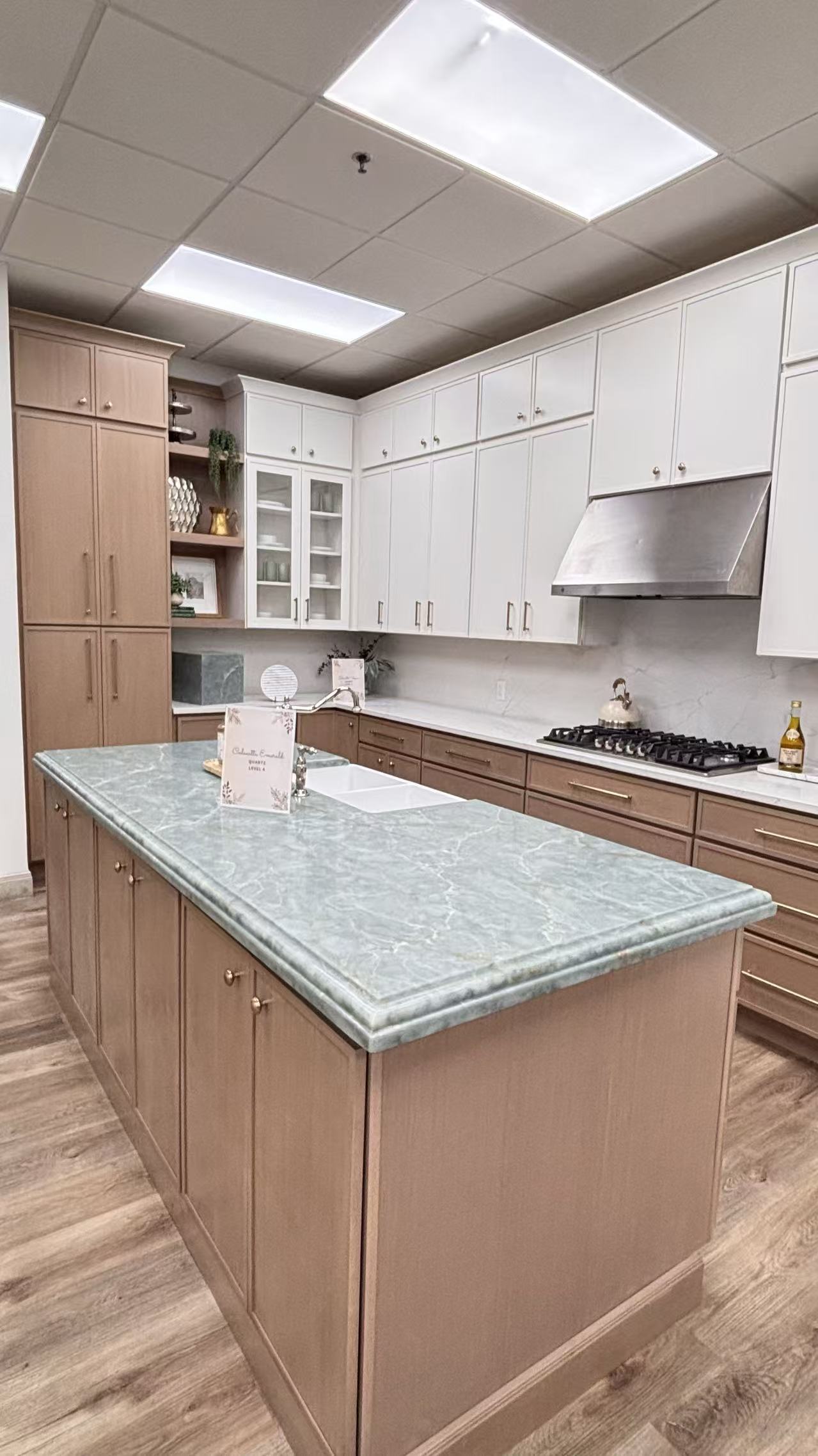 Modern kitchen corner with gray cabinetry, glass-front upper cabinets with glasses, a white hexagonal tile backsplash, and countertop holding a coffee maker, electric kettle, mugs, and a paper towel roll.