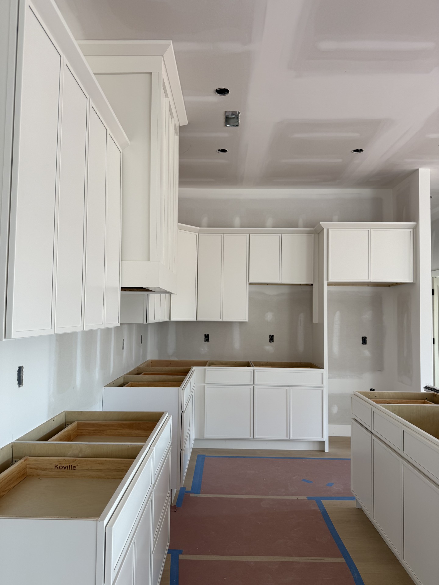 Modern kitchen with dark wood cabinets, white countertops, a large island with a gold faucet, stainless steel appliances, subway tile backsplash, and a gold chandelier with eight shades.