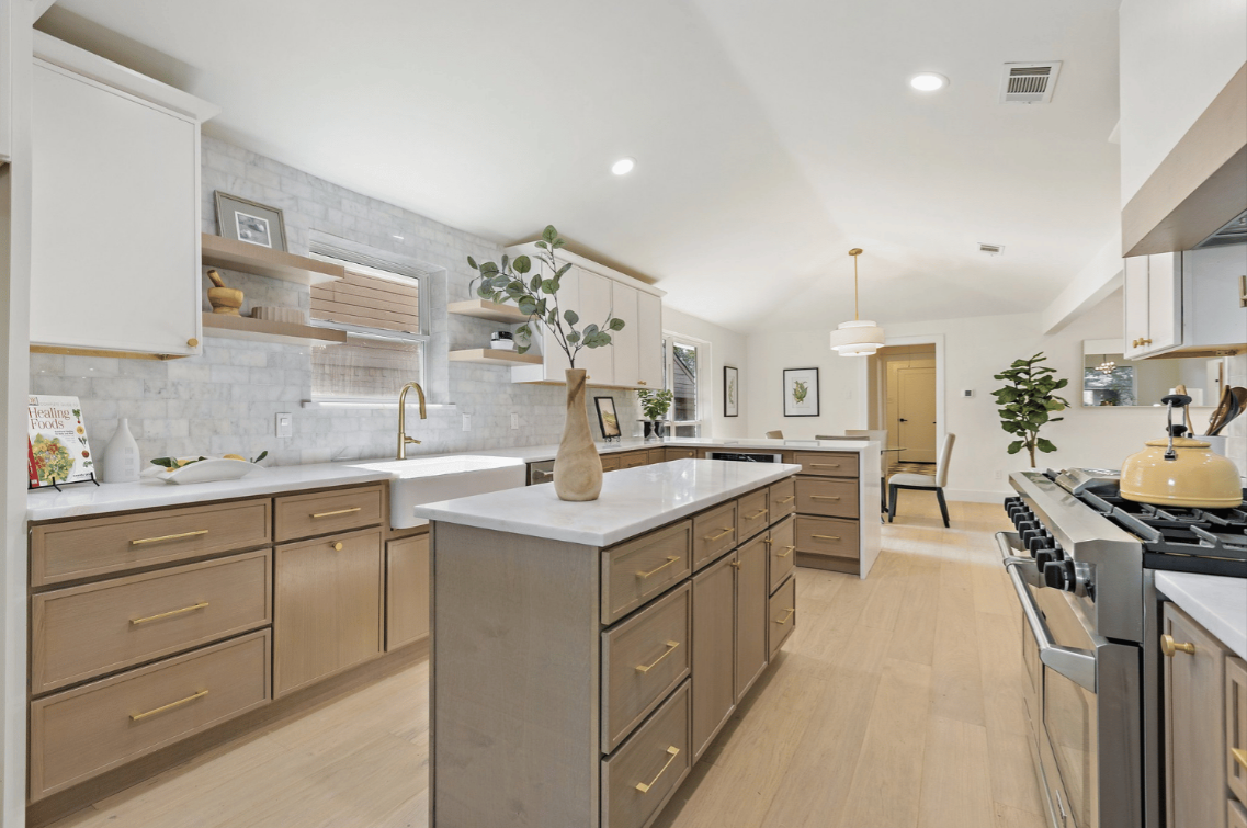 Gray kitchen cabinetry with a built-in wine rack holding three bottles and four hanging wine glasses above a stainless steel faucet and white countertop.