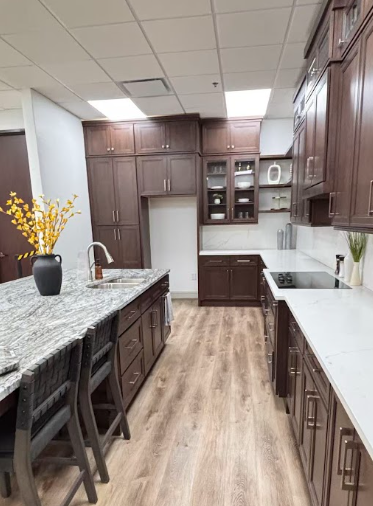 Modern kitchen with dark wood cabinets, white countertops, stainless steel double ovens, gas stove, and a large island with a sink and gold fixtures.