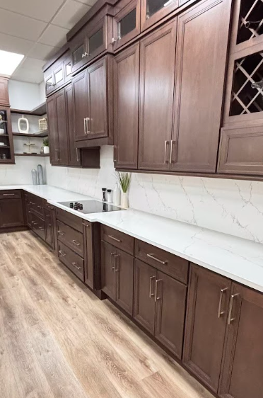 Modern kitchen with dark wood cabinets, white countertops, a large island with a gold faucet, stainless steel appliances, subway tile backsplash, and a gold chandelier with eight shades.
