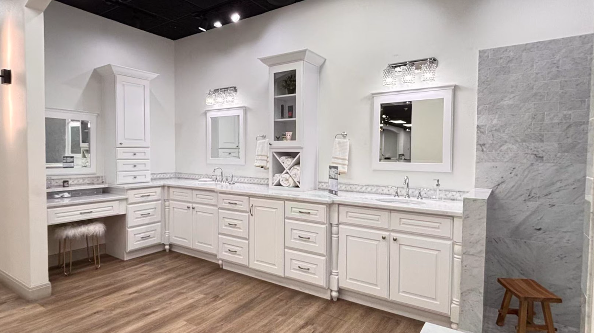 Gray kitchen cabinetry with a built-in wine rack holding three bottles and four hanging wine glasses above a stainless steel faucet and white countertop.