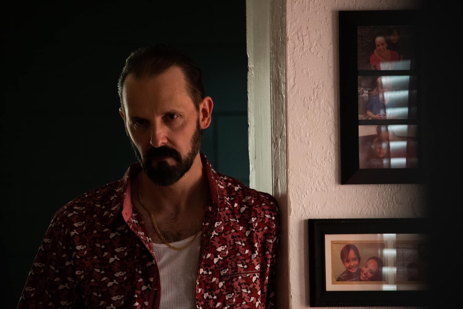 Two people indoors, a man holding a knife with a focused expression and a woman in a black leather jacket examining a knife.