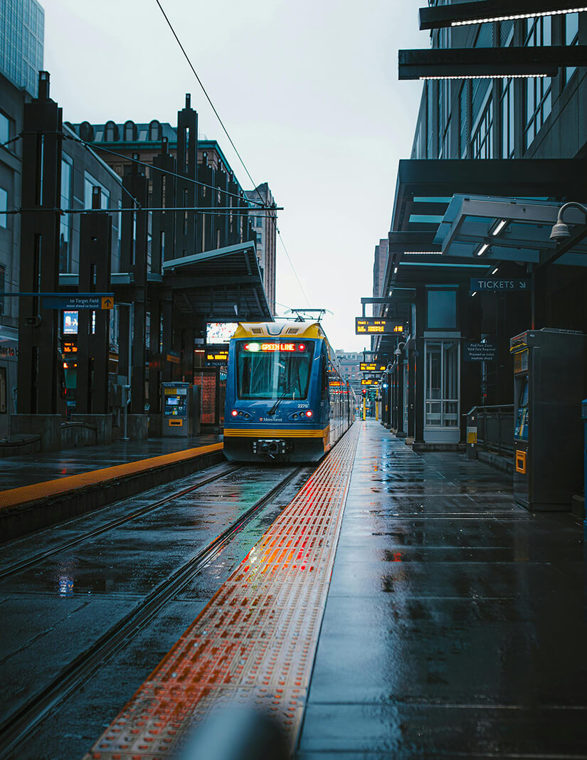 Blue and yellow light rail train labeled Green Line arriving at a wet urban train station platform.