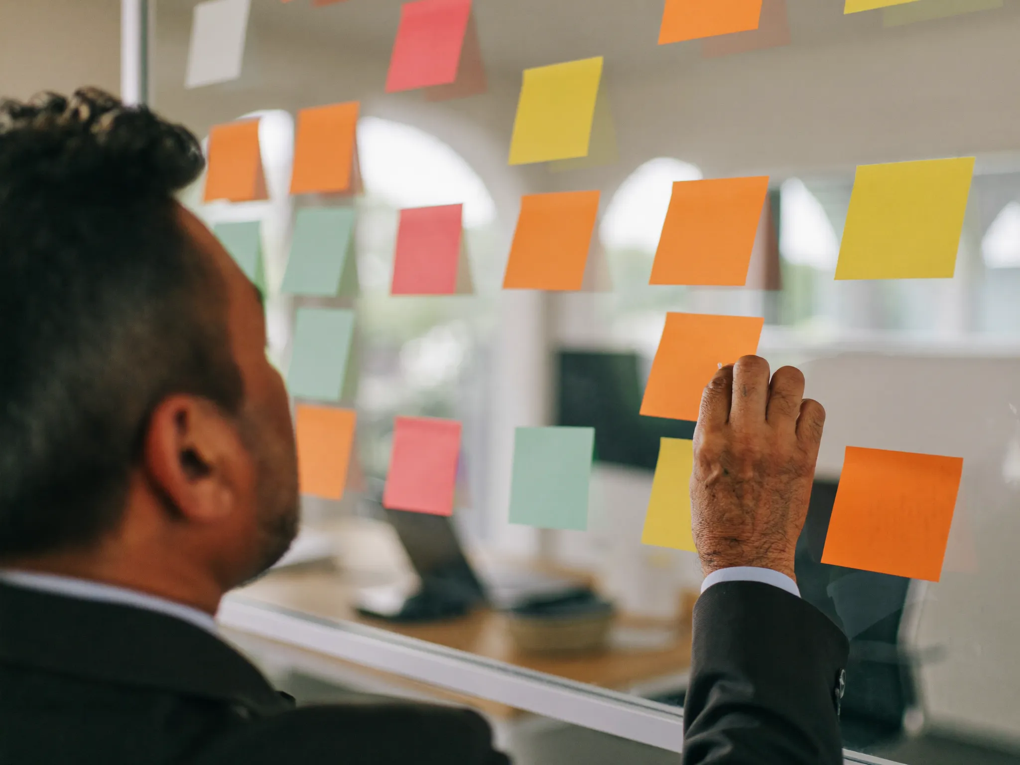 Senior Latin American marketing director arranging team role sticky notes on a glass office wall