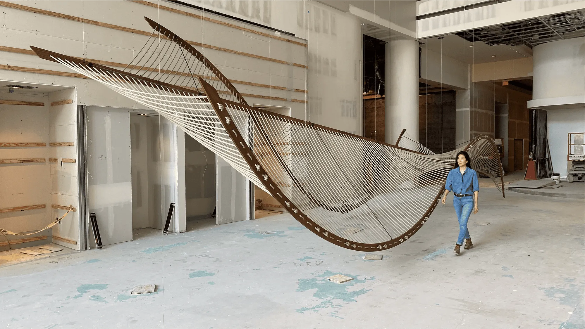 artist walking next to large hanging sculpture made of wood and rope