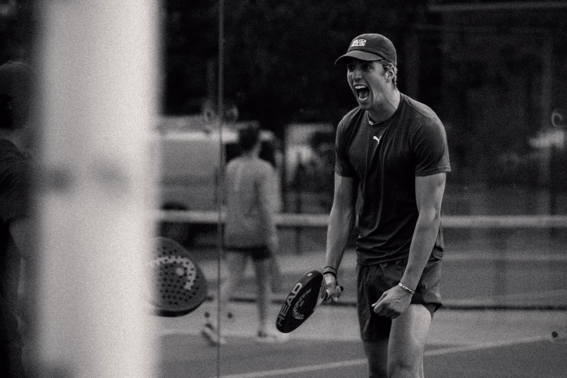 Man shouting energetically during a paddle tennis game, holding a paddle racket in one hand.