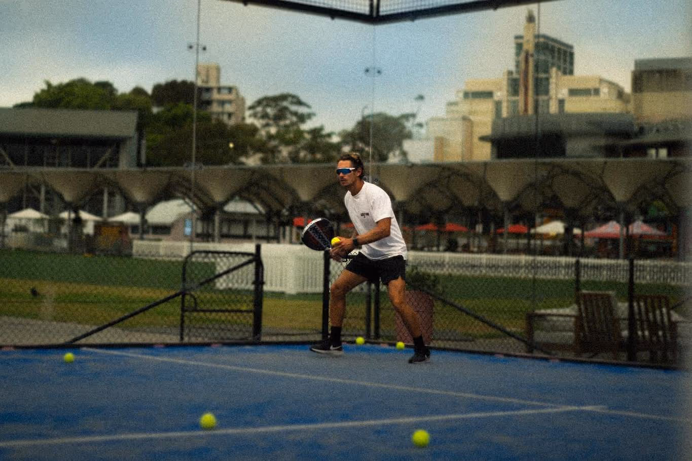 Man wearing a white t-shirt and black shorts playing paddle tennis on a blue court.