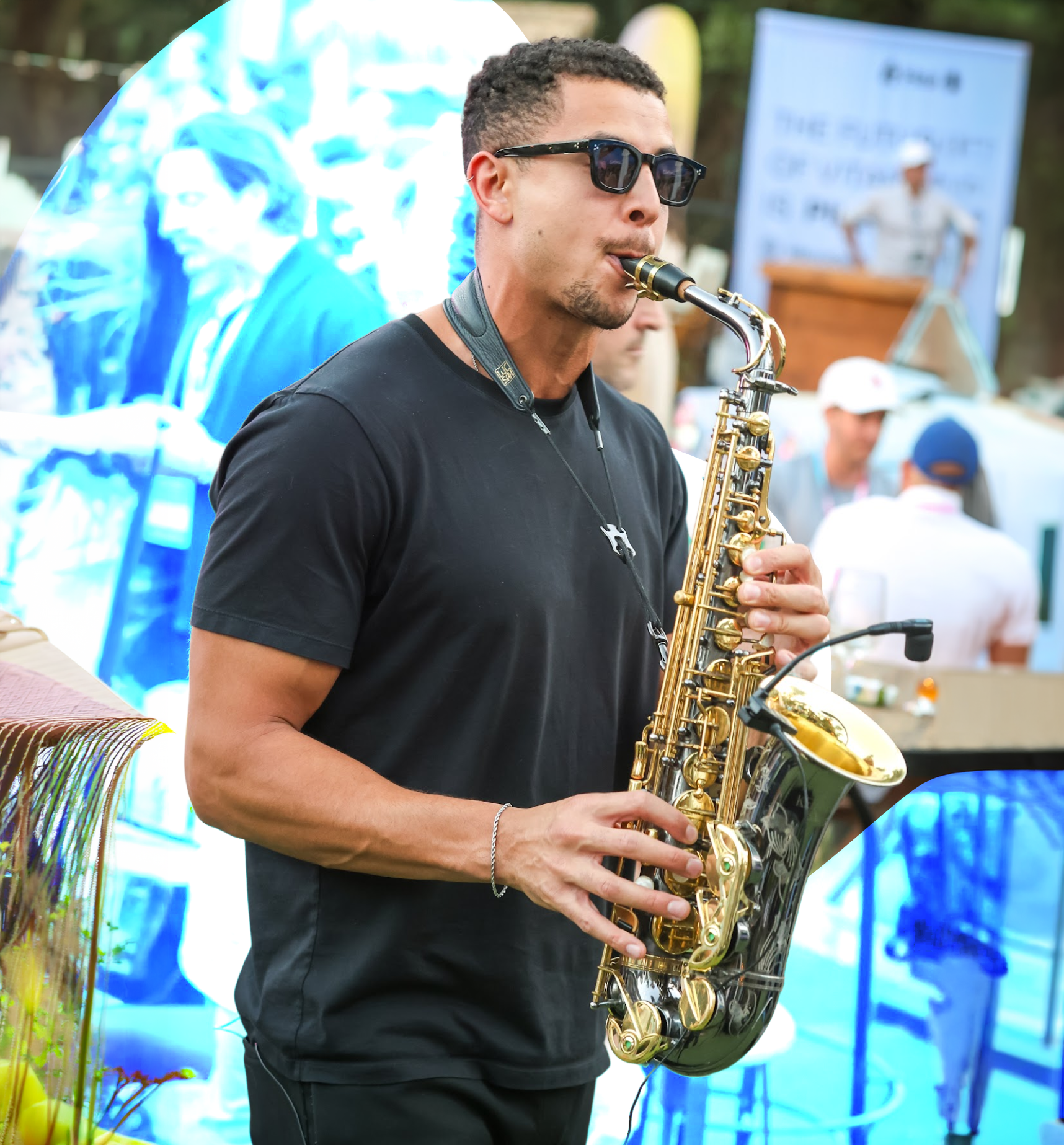 Man wearing sunglasses playing a saxophone outdoors at an event.