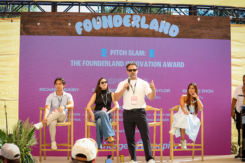 Four speakers on stage at Foundreland Pitch Slam event with a large purple presentation screen behind them.