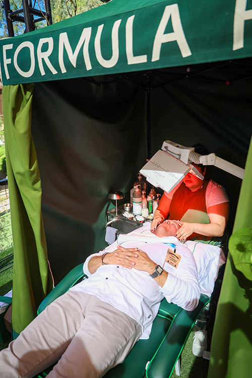 Person receiving a facial treatment on a reclining chair inside a green tent with 'FORMULA' partially visible on the canopy.