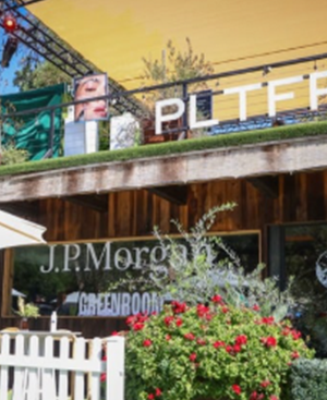 Outdoor stage setup with J.P. Morgan and Greenbook logos on the backdrop and a white fence and red flowers in front.