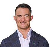 Smiling man with short dark hair wearing a dark checked blazer and white collared shirt.