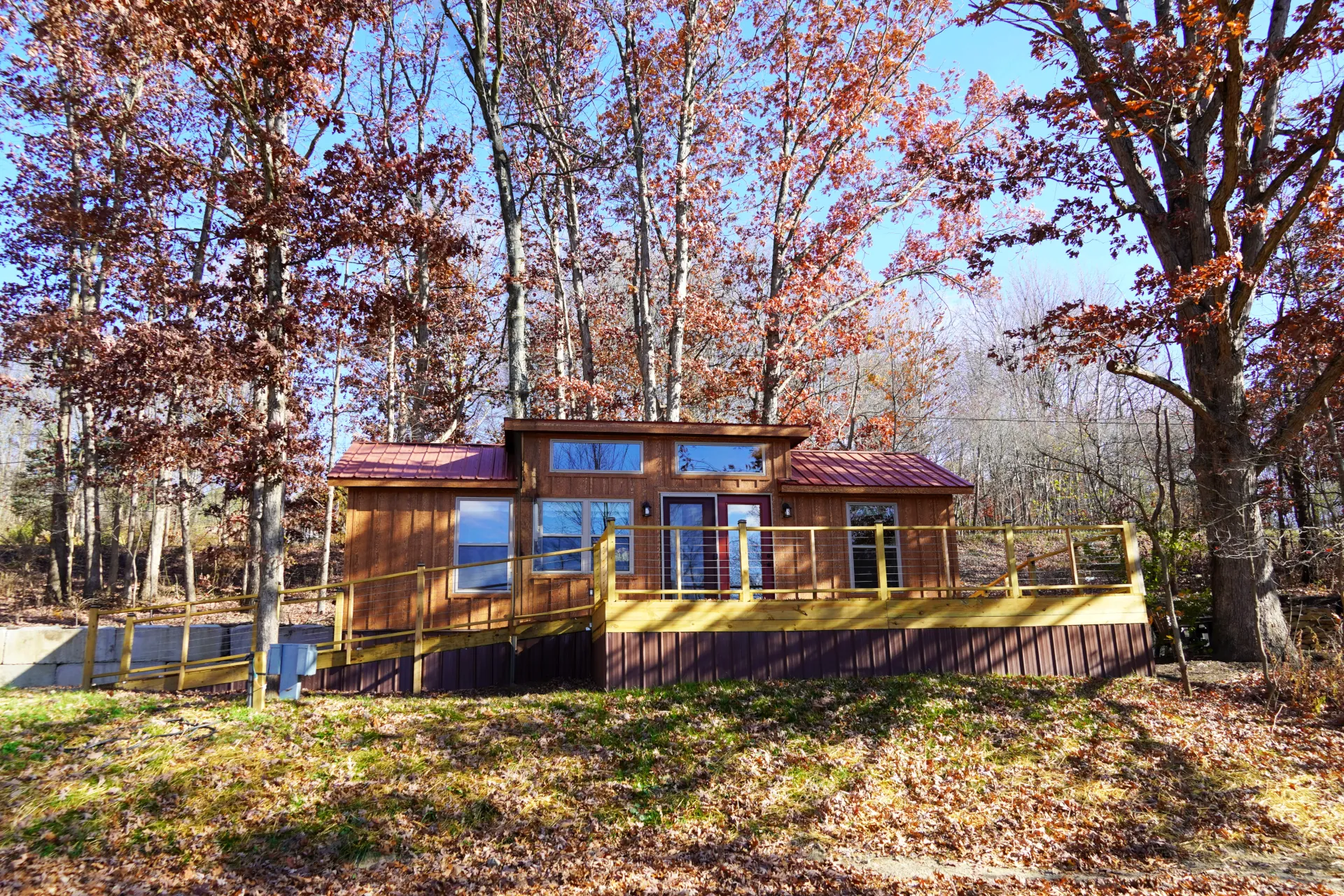 Amish-built tiny home with a wooden exterior, metal roof, and spacious deck surrounded by trees.