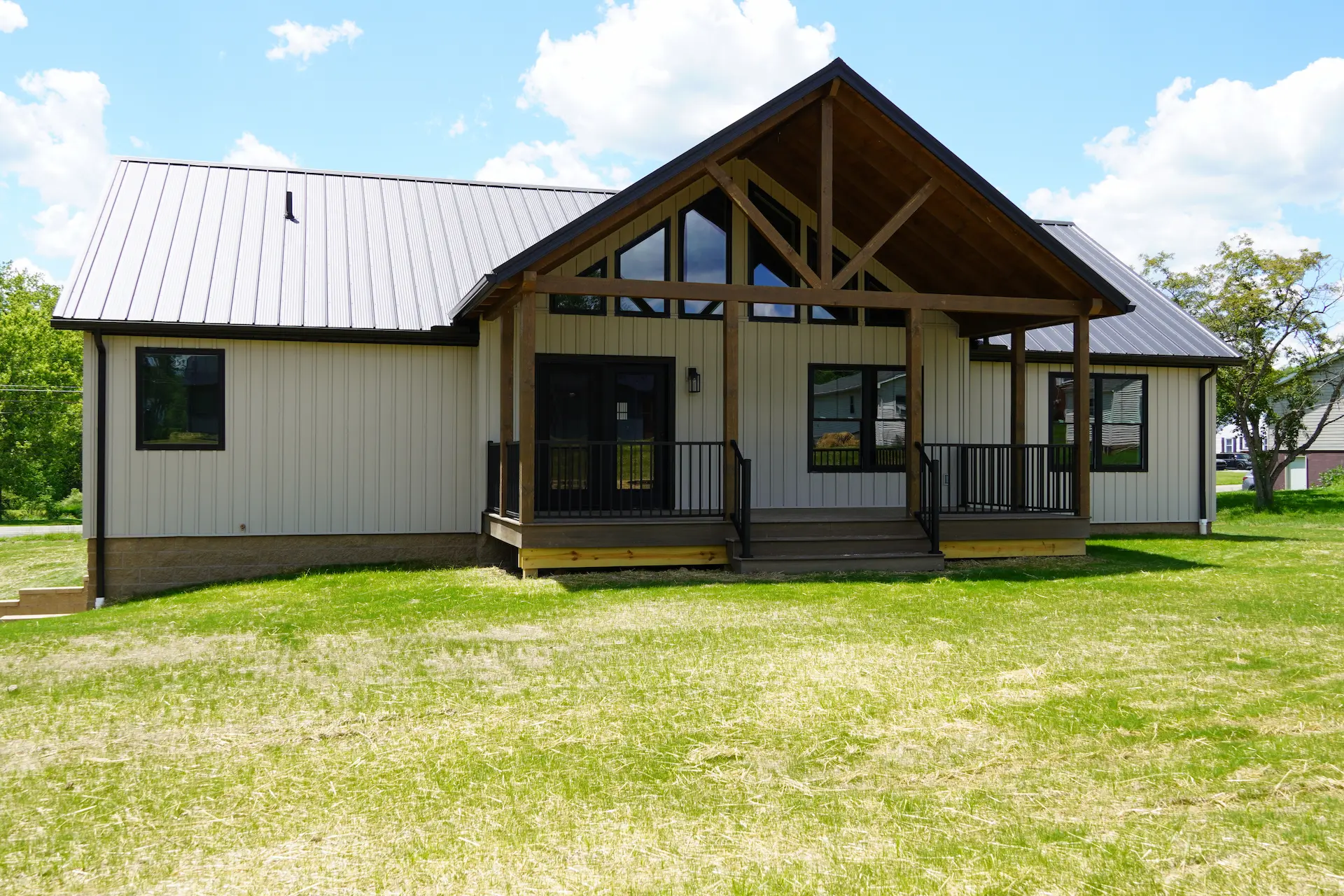 Farmhouse-style modular home by Buckhorn Showcase featuring white vertical siding, a metal roof, black-framed windows, and a covered timber-frame front porch.