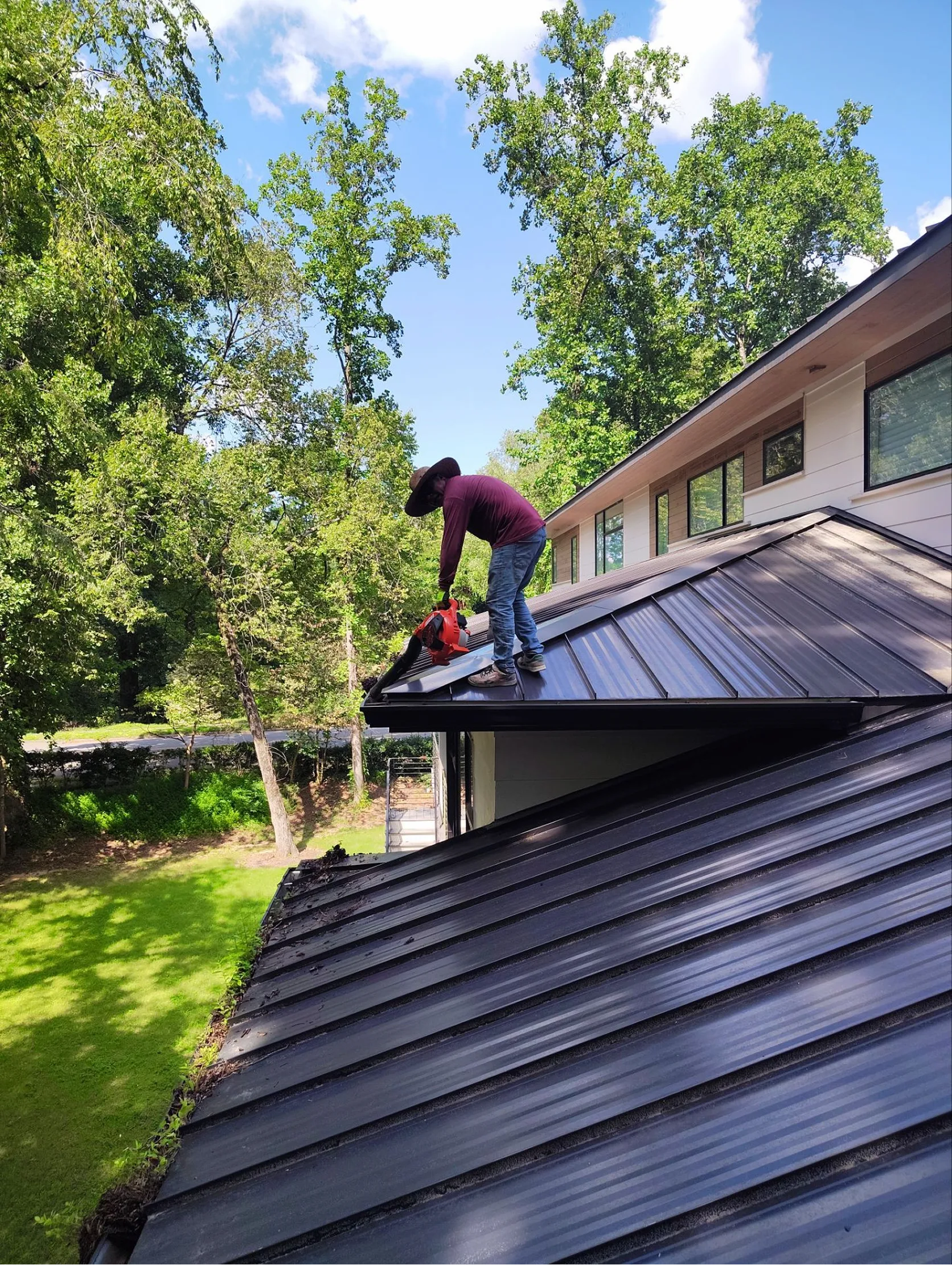 Roofing professional clearing leaves from metal roof gutters on a residential home in Raleigh, North Carolina.