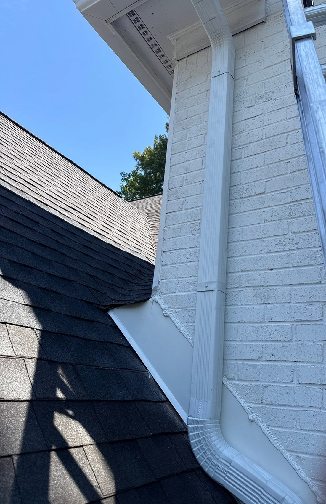 White aluminum downspout and gutter system installed along a residential home exterior for proper water drainage.