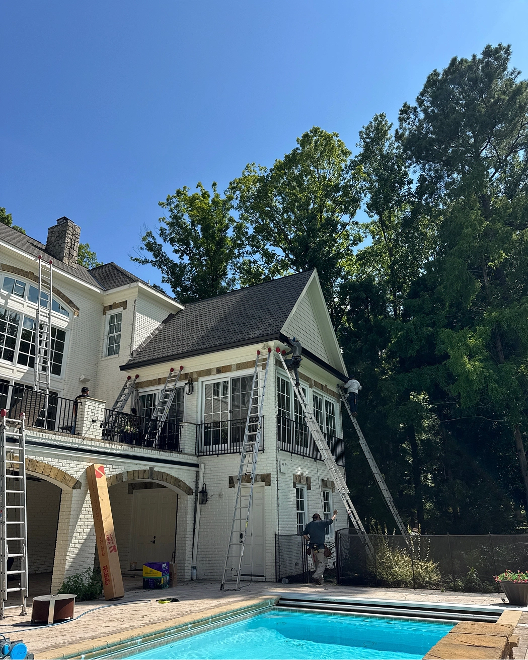 Multiple technicians installing a new gutter system on a large residential home during a professional exterior project.