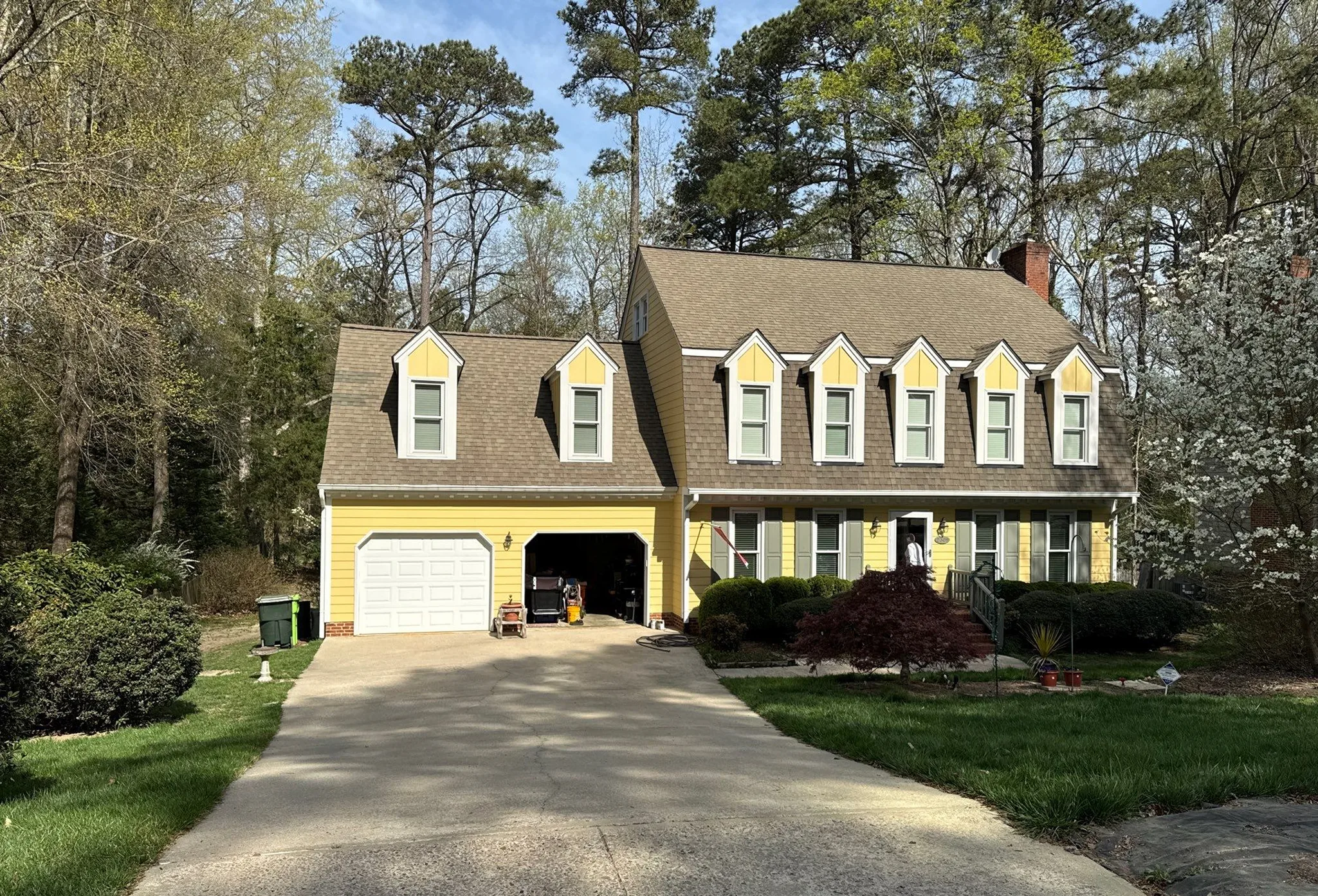 Front exterior of a yellow residential home with dormer windows and updated window trim.