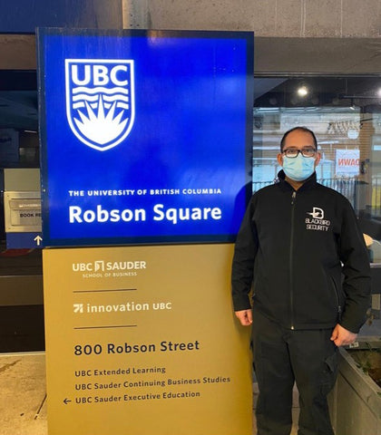 Uniformed Blackbird security guard in front of Robson square sign in Vancouver, BC