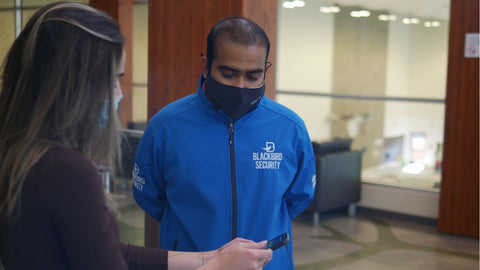 Uniformed Blackbird security guard speaking to woman in office
