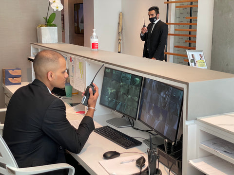 two security guards speaking on radios and looking at CCTV screens in reception area