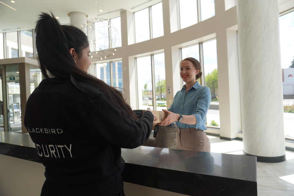 Condo concierge security guard hands a package to a resident at the front desk.