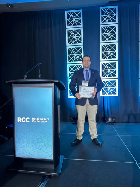 Amir Anzivaradez stands on a stage the Retail Secure Conference with his award for outstanding retail security.