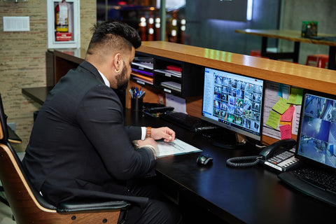 Uniformed Blackbird security guard sitting at reception desk in front of screen