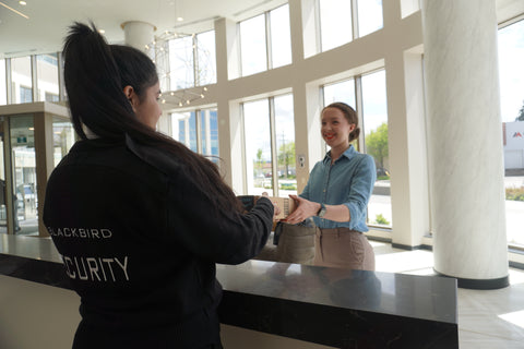 Uniformed Blackbird security guard at concierge desk handing a woman a package