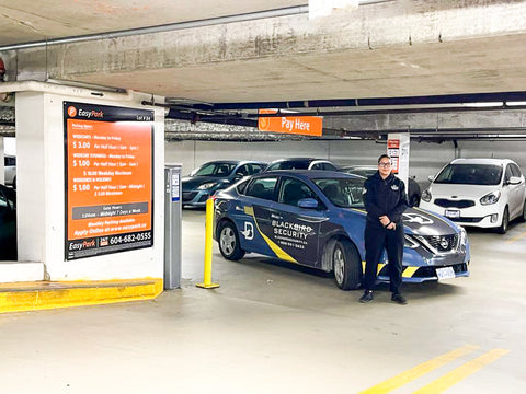 Uniformed Blackbird security guard in front of Mobile in parkade patrol car