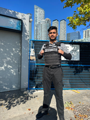Blackbird security guard with hands stuffed in tactical vest in front of office towers