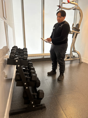 Uniformed Blackbird security guard standing in front of barbells with clipboard