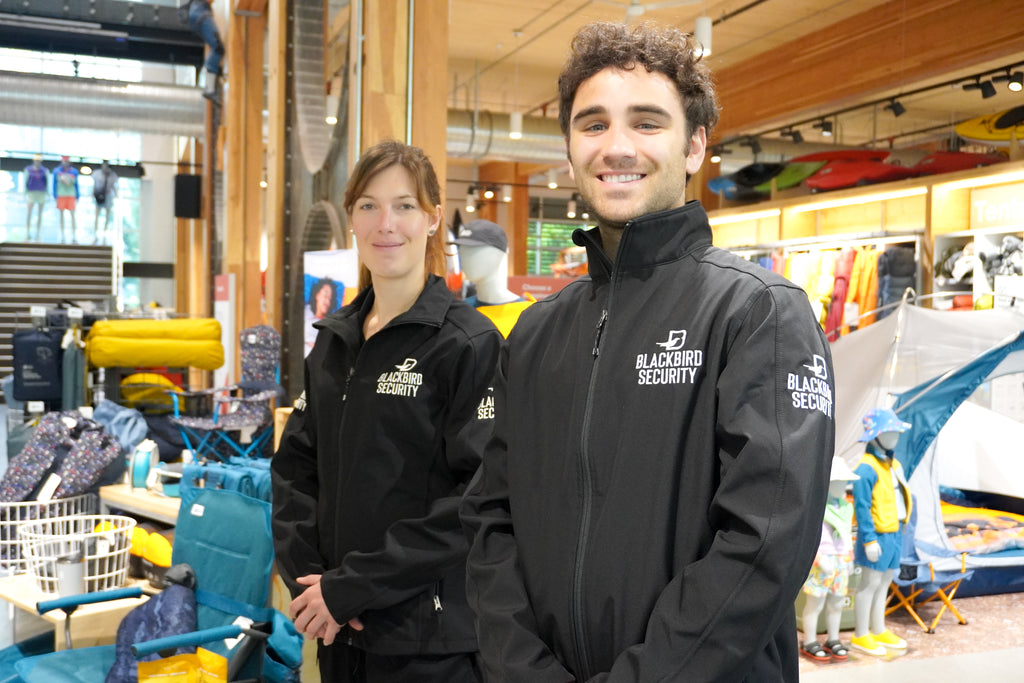 Two people wearing Blackbird Security jackets in a store setting.