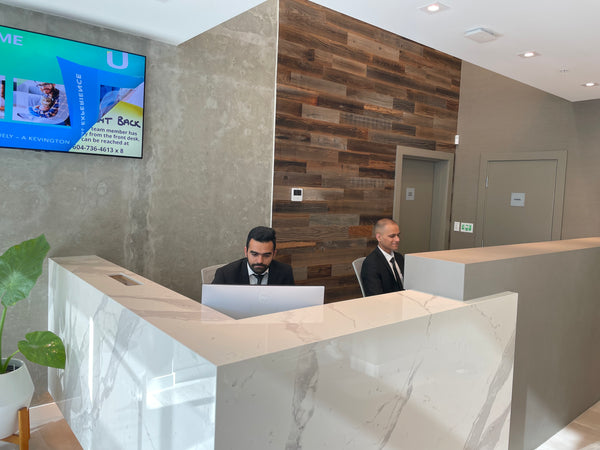 Uniformed Blackbird security guard sitting at concierge desk in front of two security camera screens