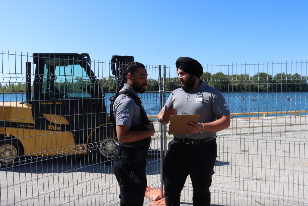Two men standing near a forklift with a body of water and trees in the background