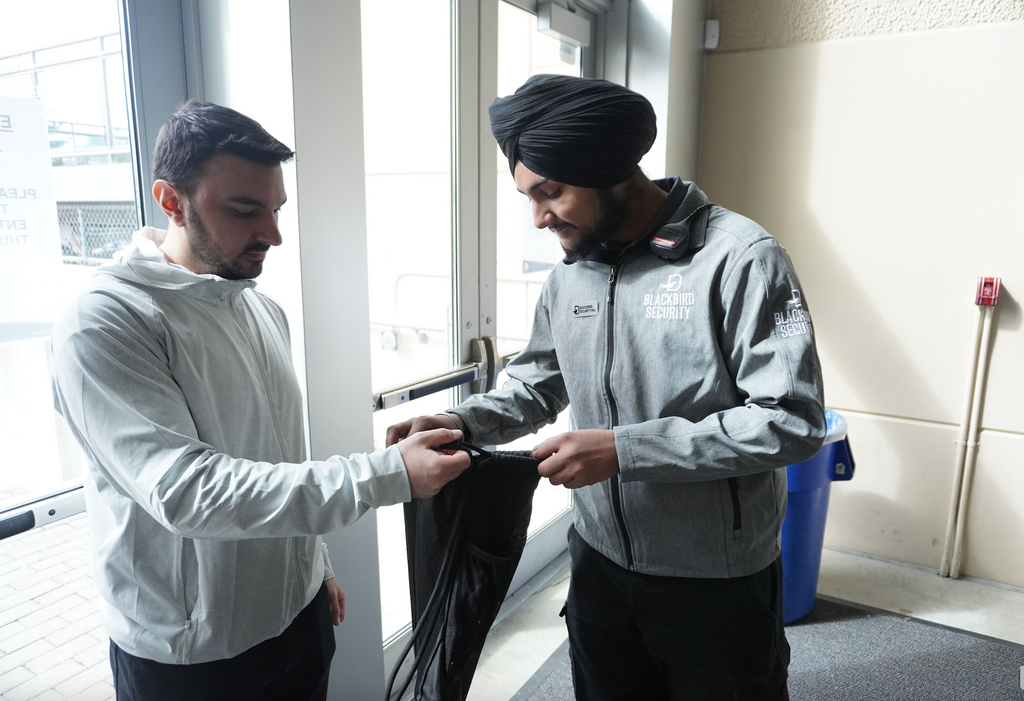 A Blackbird Security event security guard looks inside of a man's black drawstring backpack during a bag check.