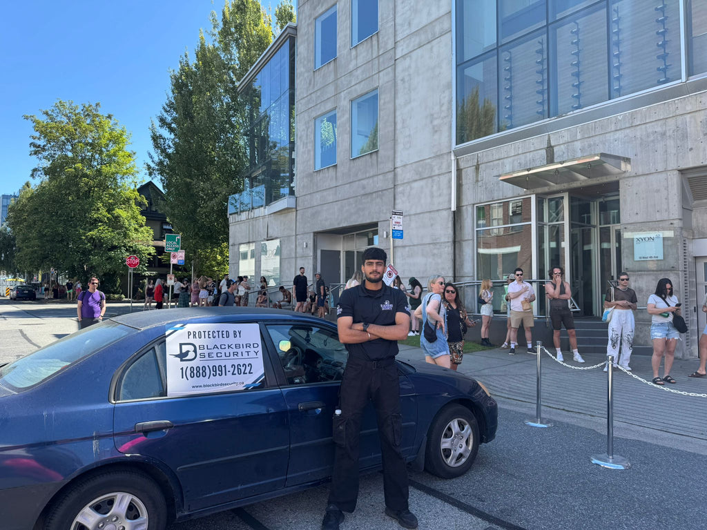 A Blackbird Security mobile patrol security guard stands in front of a marked security vehicle at a Pride weekend event at The Birdhouse in Vancouver.