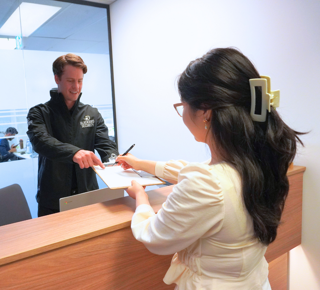 Security officer is asking a visitor to sign the document on a clipboard at the desk of a corporate office building.