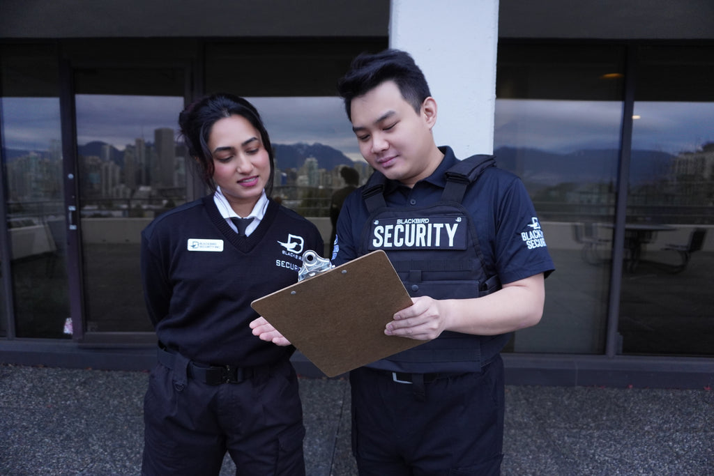 Two Blackbird Security guards stand outside of a building reviewing a clipboard.