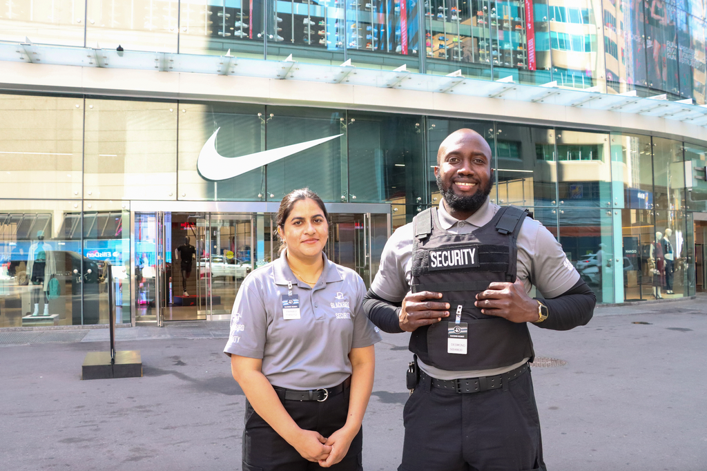 Two security personnel standing in front of a building with a visible brand logo.