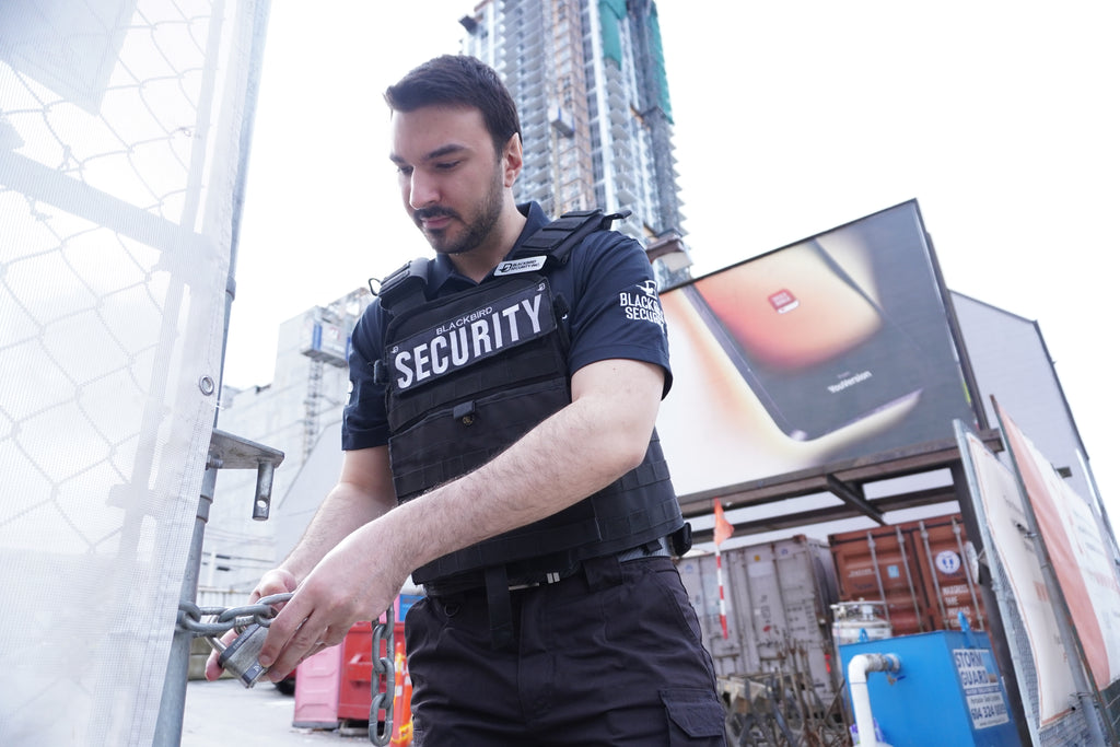 Security guard in a city setting with buildings and a large screen in the background