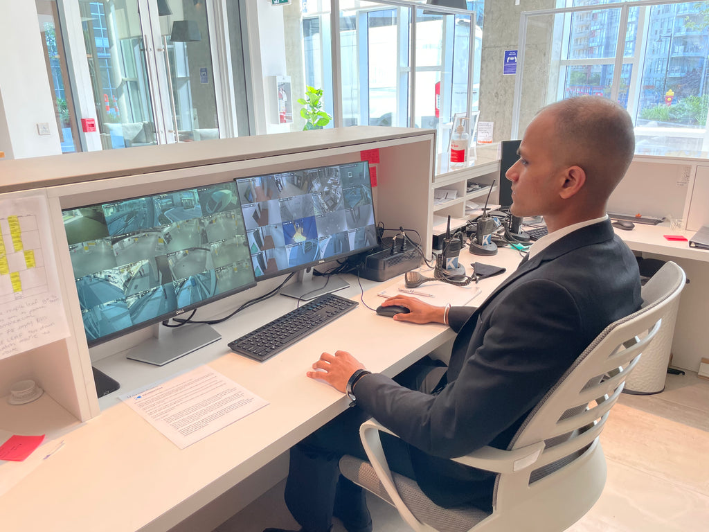 A concierge security guard sitting at a desk monitoring CCTV cameras