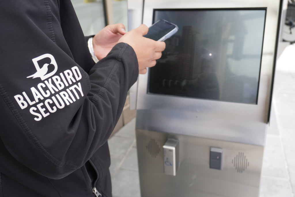 Security guard stands at a buzzer terminal making a report on their phone