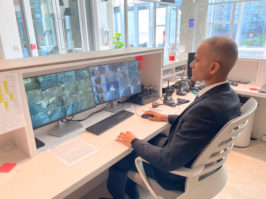 A security guard sits at a front desk monitoring CCTV feeds.