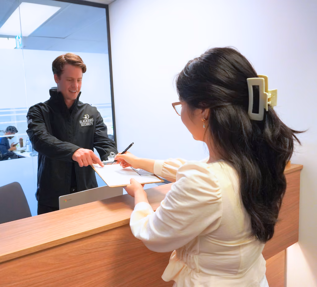 Security officer is asking a visitor to sign the document on a clipboard at the desk of a corporate office building.